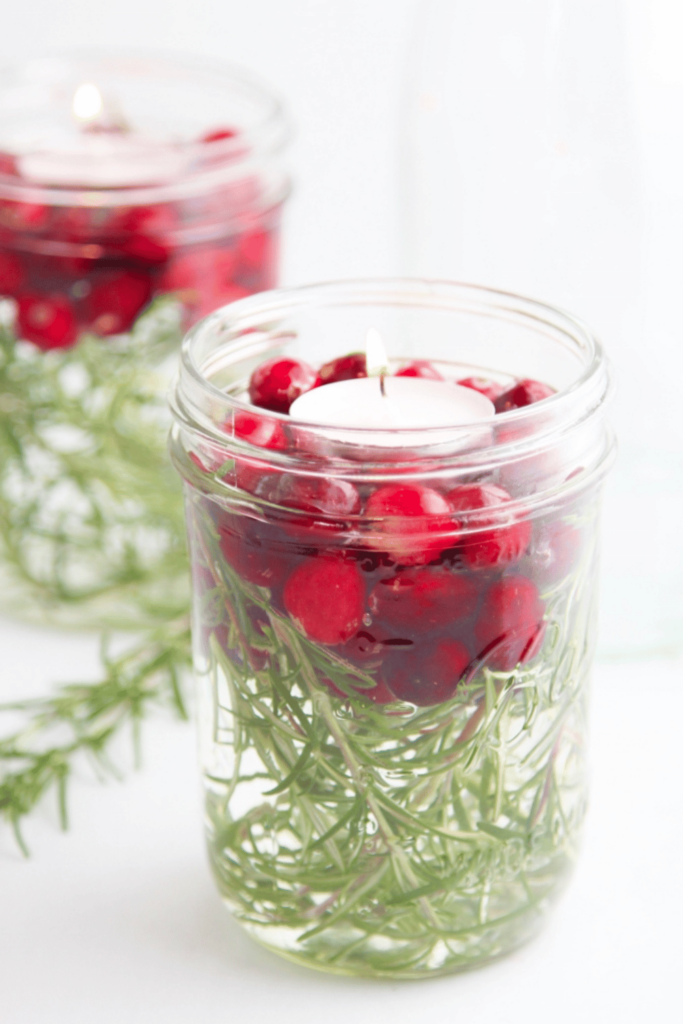 Mason jar filled with water, rosemary, cranberries and a tea light candle