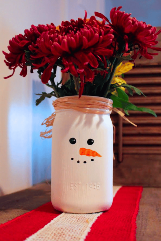 A mason jar painted white with a cute snowman face