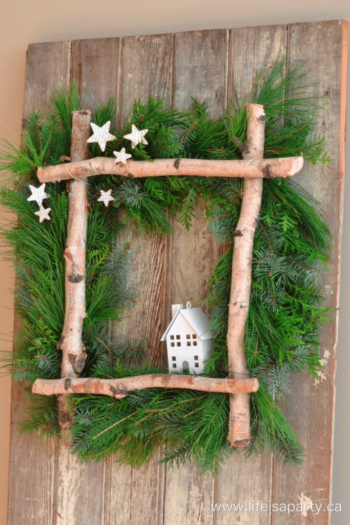 A unique square shaped wreath made using tree branches, handmade stars and a little white house