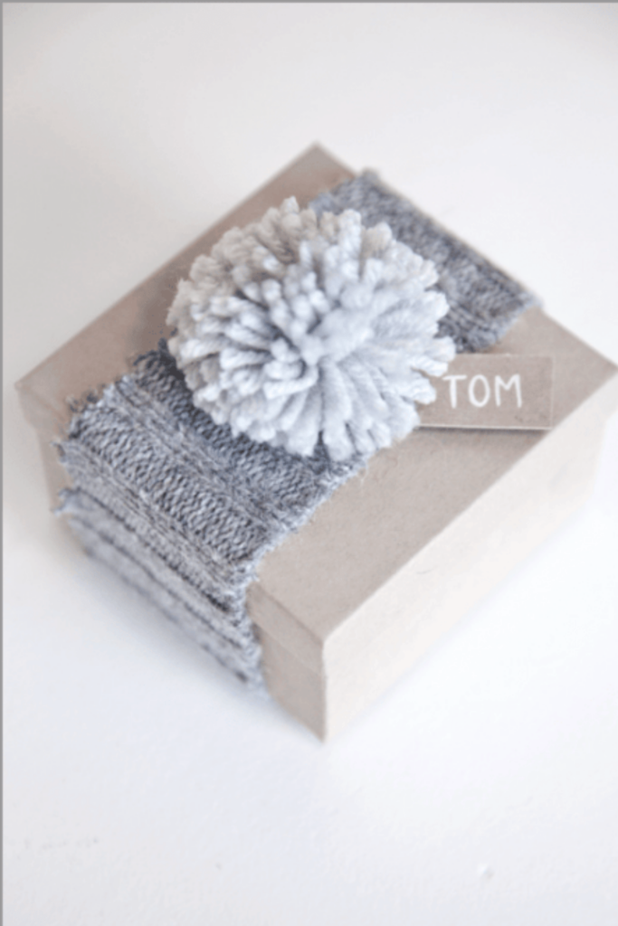 A small box sealed with a knitted ribbon and pom pom top