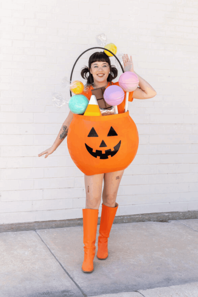 Woman wearing a Halloween candy bucket costume with oversized candy props and matching orange boots.