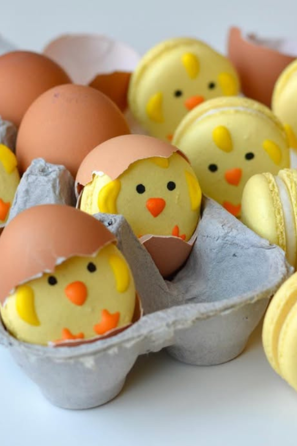 Yellow macarons with cute chick faces, nestled inside cracked eggshells in an egg carton.