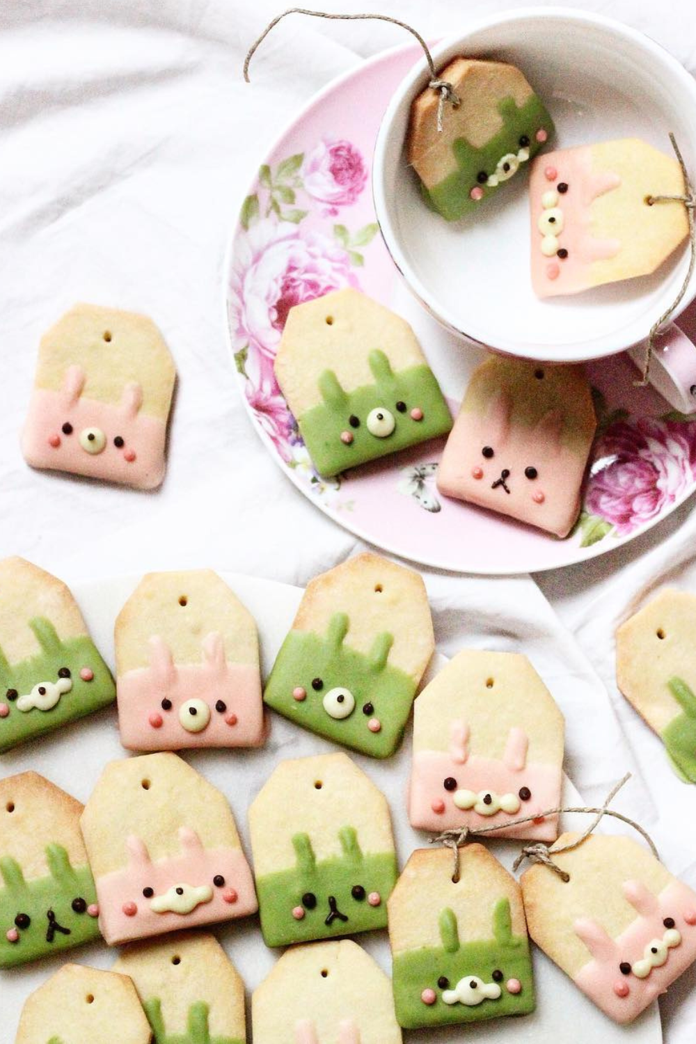 Tea bag-shaped cookies dipped in strawberry and matcha icing, designed with bunny faces and tied with twine.