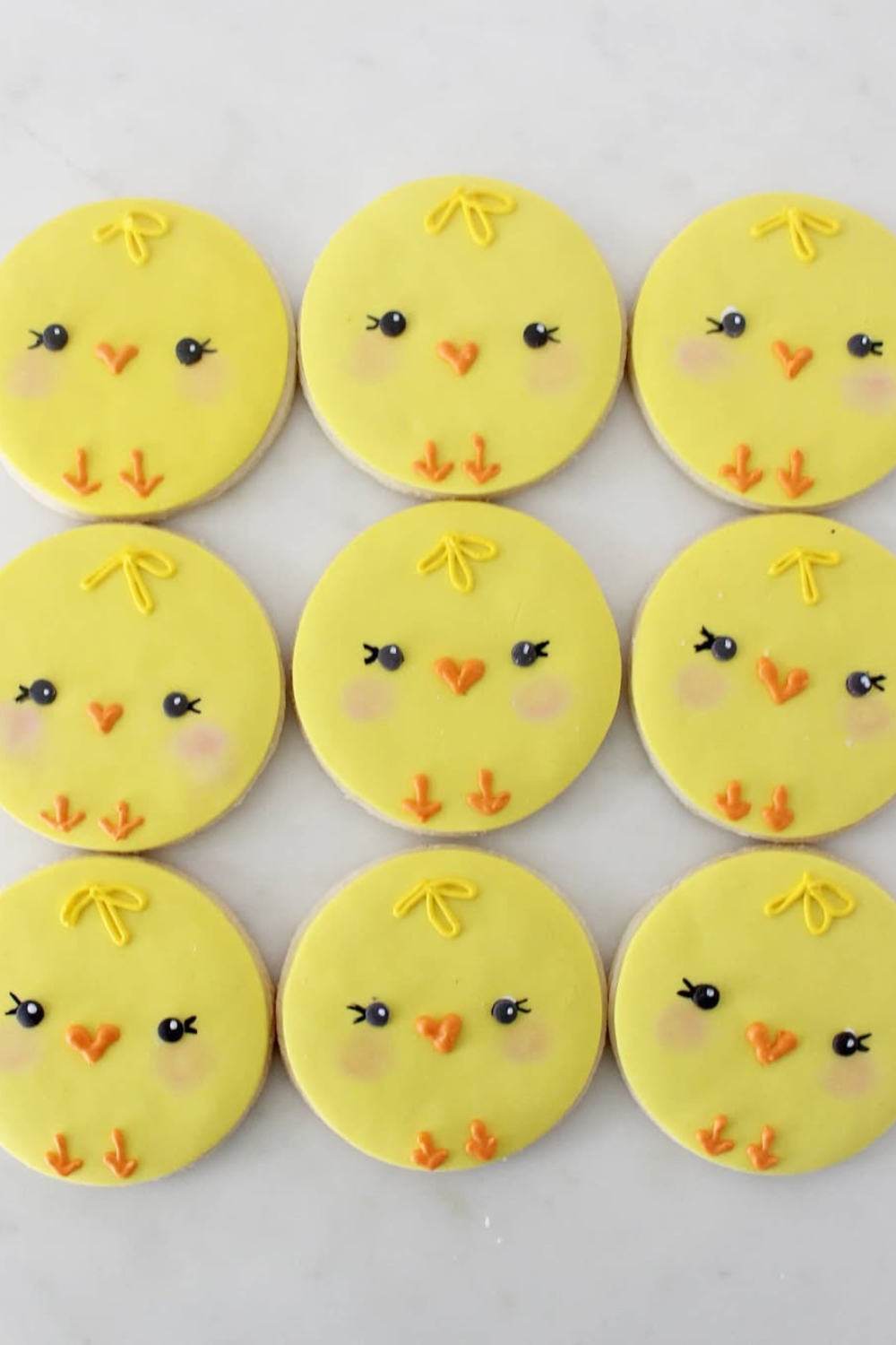 Round yellow sugar cookies with baby chick faces, decorated with rosy cheeks and orange beaks.