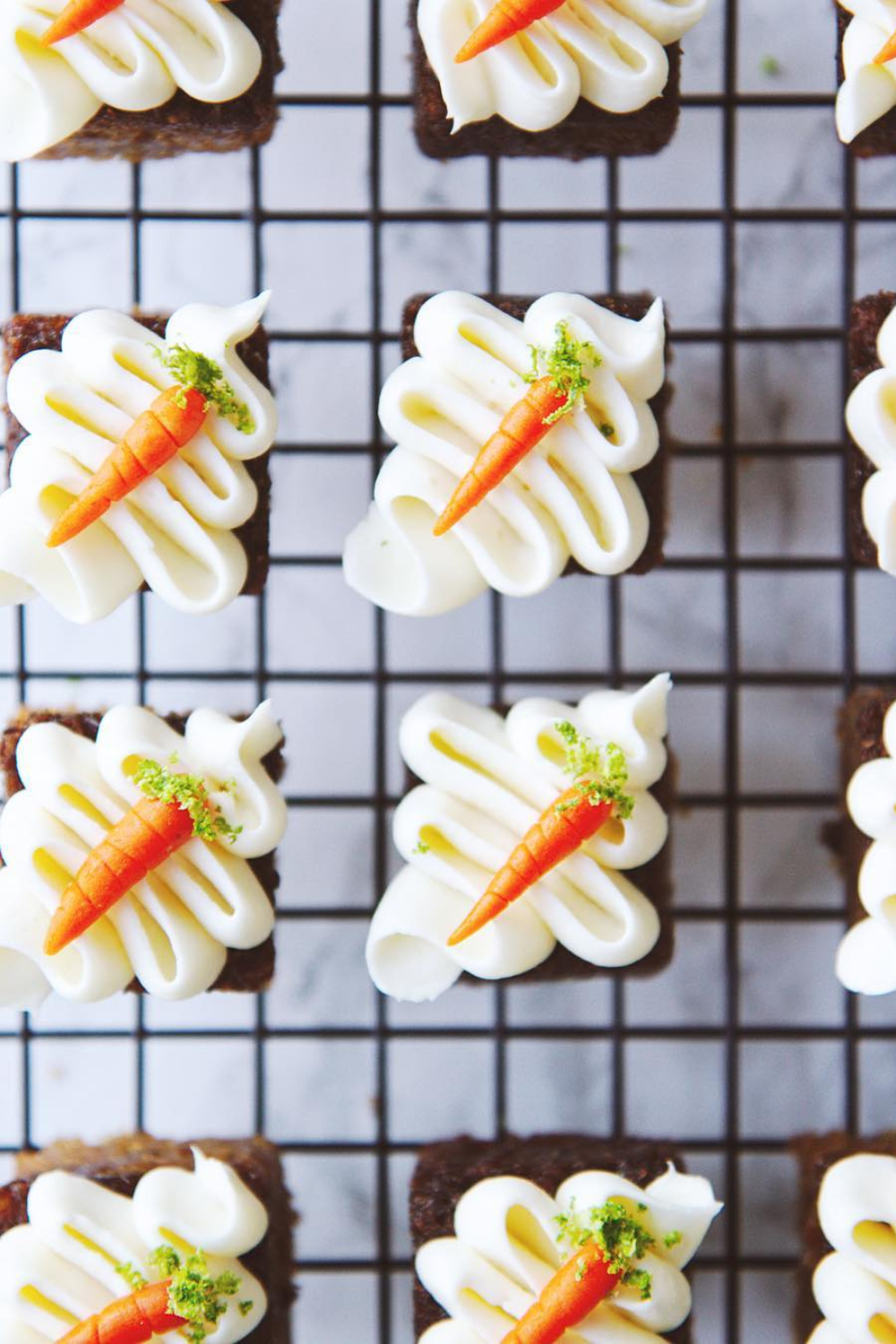 Bite-sized carrot cakes topped with piped white frosting and tiny edible carrot decorations.