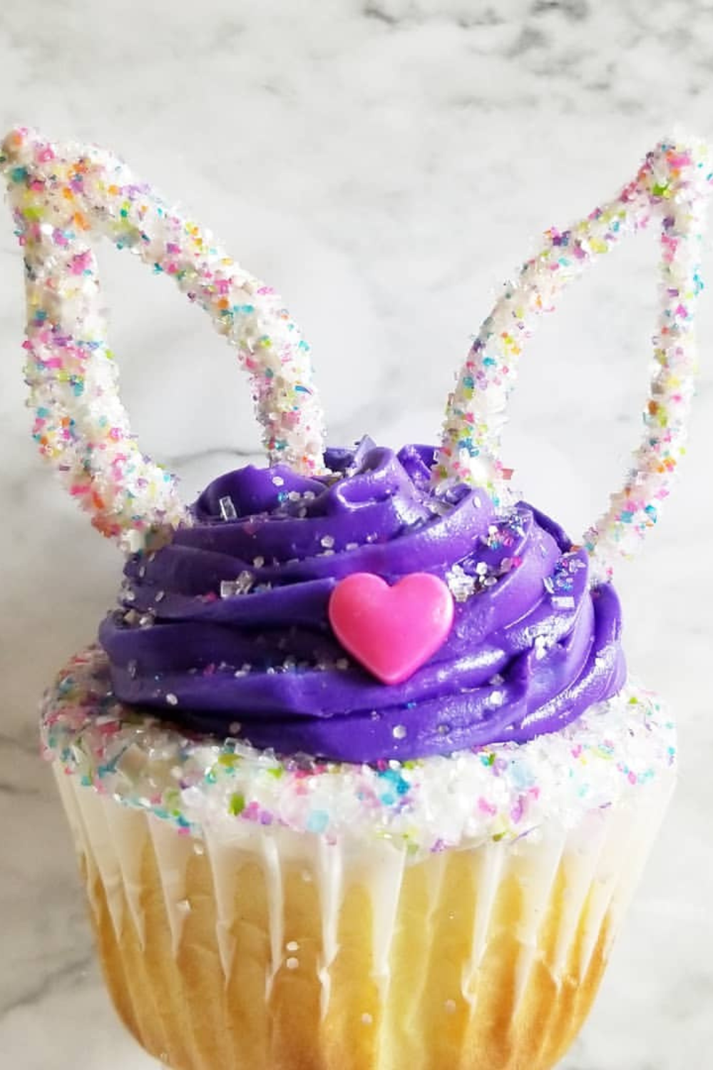 Cupcakes with vibrant frosting, sparkling sprinkles, and candy melt bunny ears on top.
