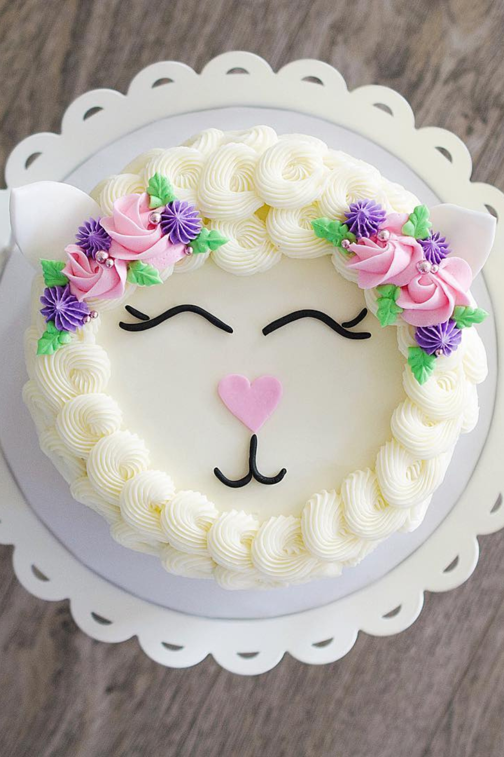 A round carrot cake decorated as a lamb, with white piped frosting and a pink heart-shaped nose.