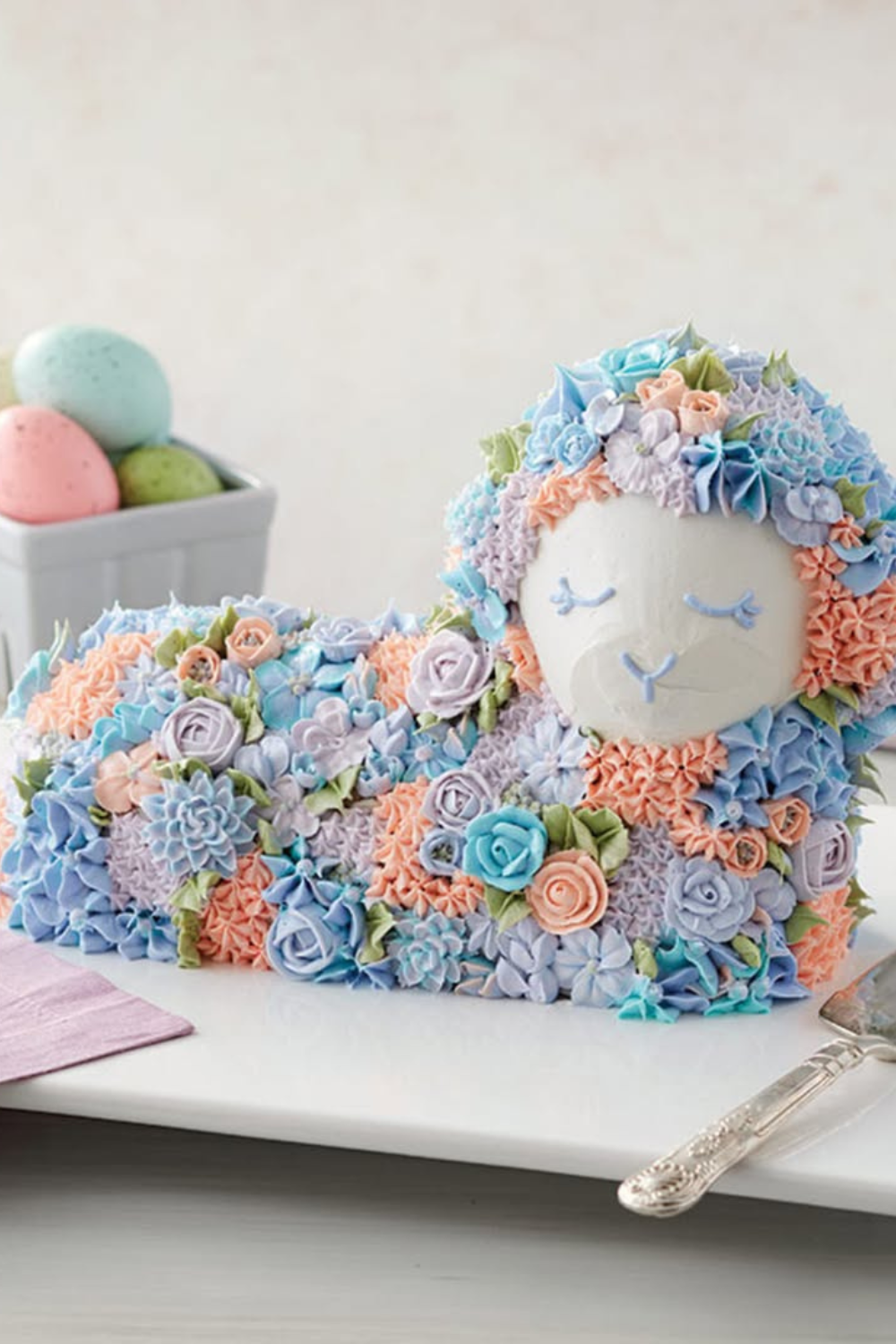 A lamb-shaped cake covered in pastel-colored frosting rosettes, surrounded by soft spring decorations.