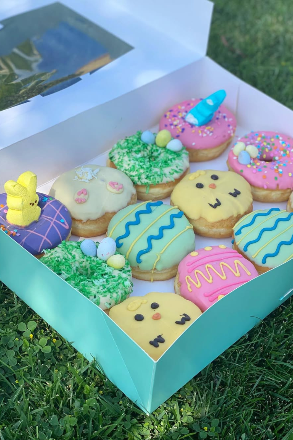A box of pastel-decorated donuts with Easter-themed designs like chicks, eggs, and sprinkles.