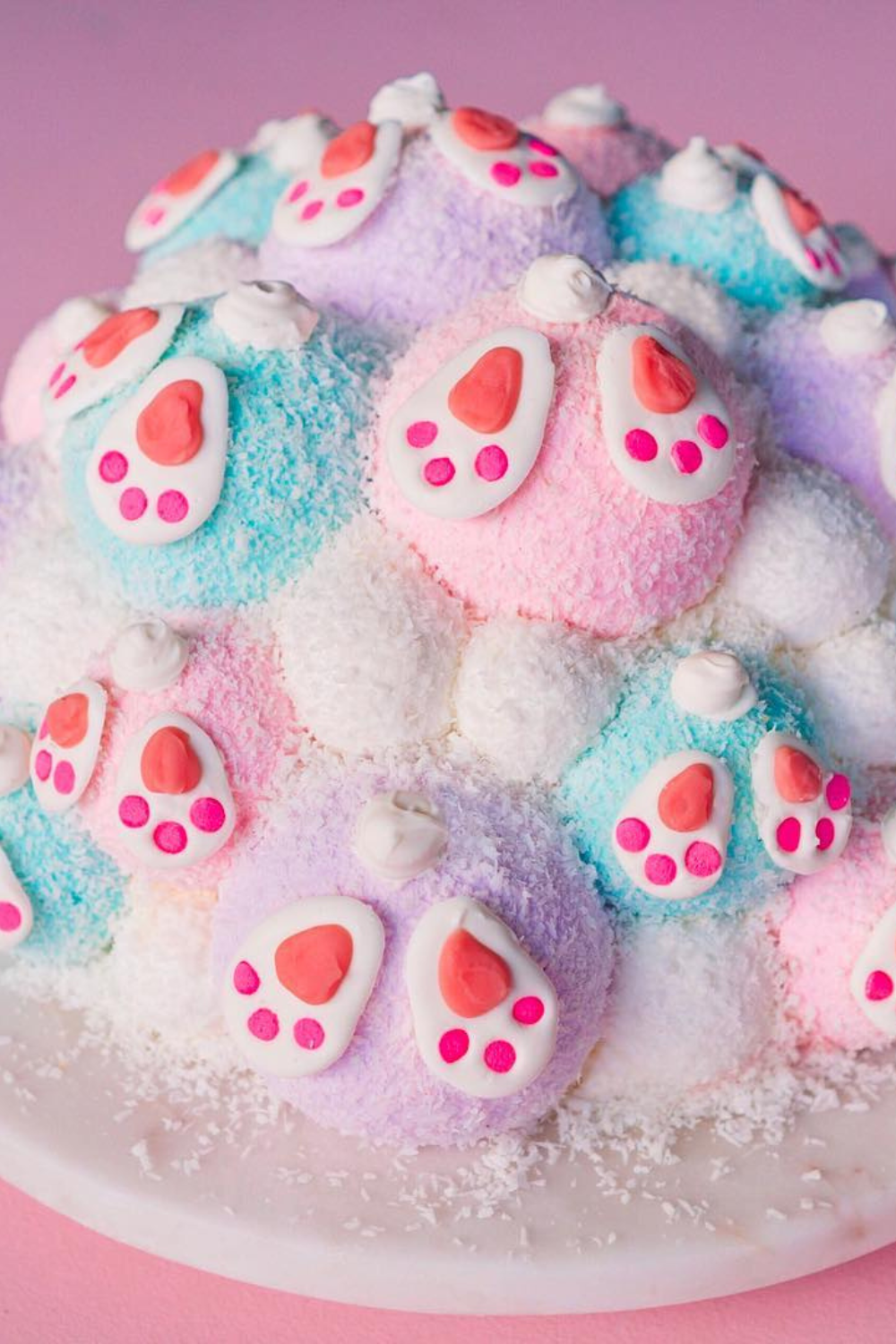 A dome-shaped cake with colorful coconut frosting and bunny feet and tail decorations on top.