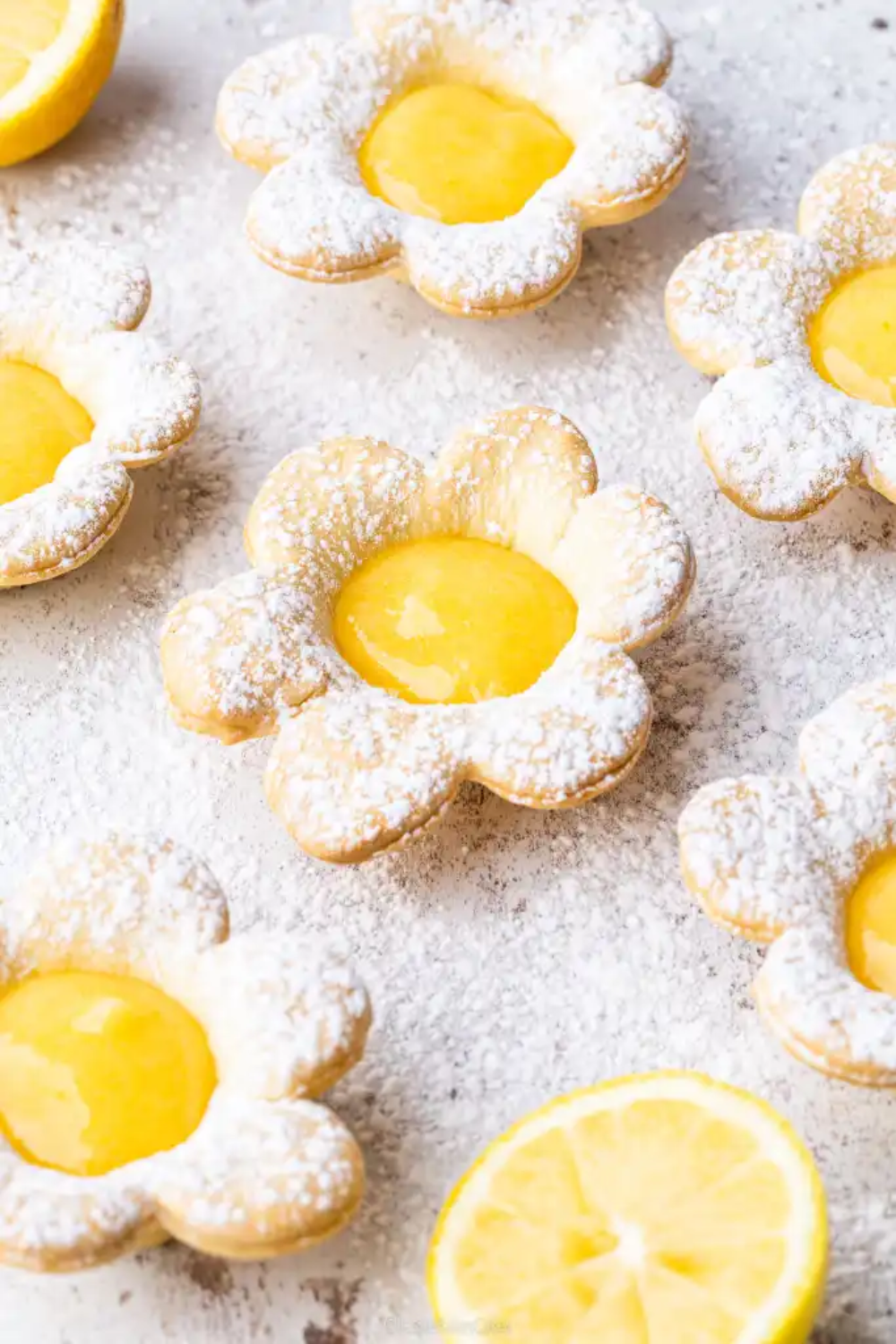 Flower-shaped tartlets with powdered sugar-dusted crusts and bright yellow lemon curd centers.