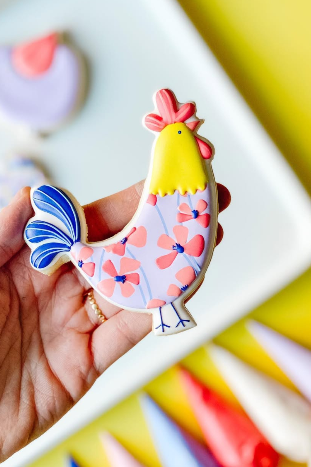 Hand-decorated chicken-shaped sugar cookies with colorful floral patterns, held in a hand.