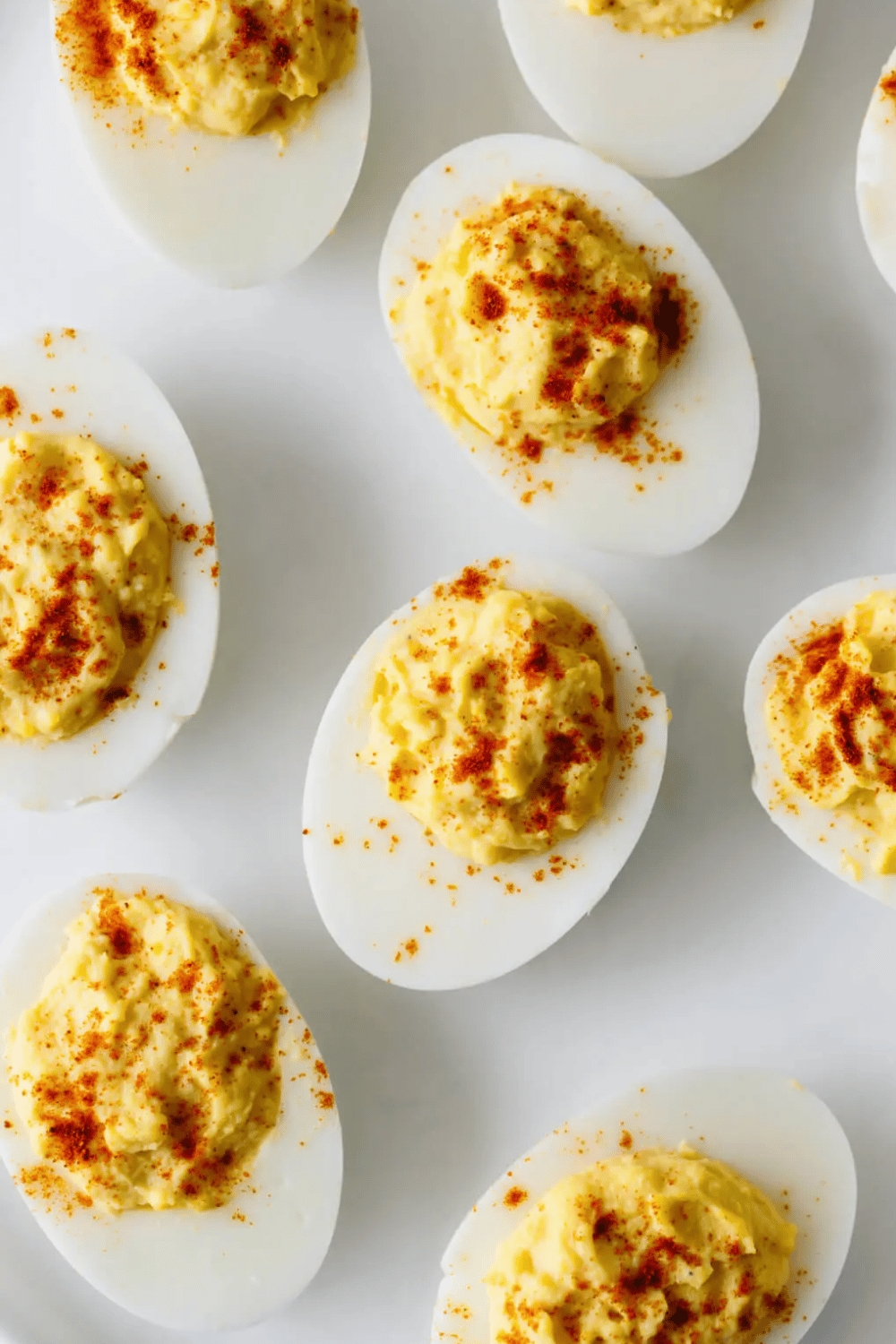 Close-up of creamy devilled eggs sprinkled with paprika, arranged on a white plate.