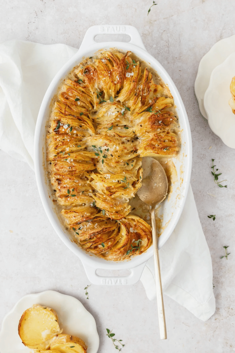 A baking dish of scalloped potatoes layered in a circular arrangement, garnished with herbs.