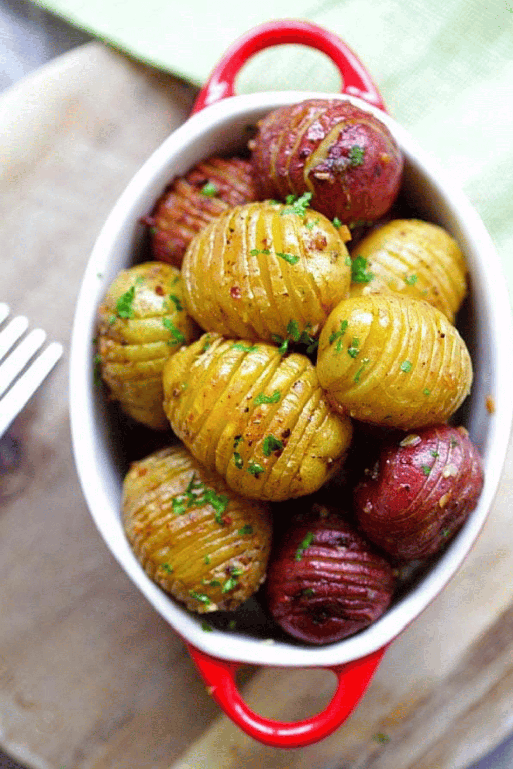 Crispy roasted new potatoes garnished with parsley in a red-handled baking dish.