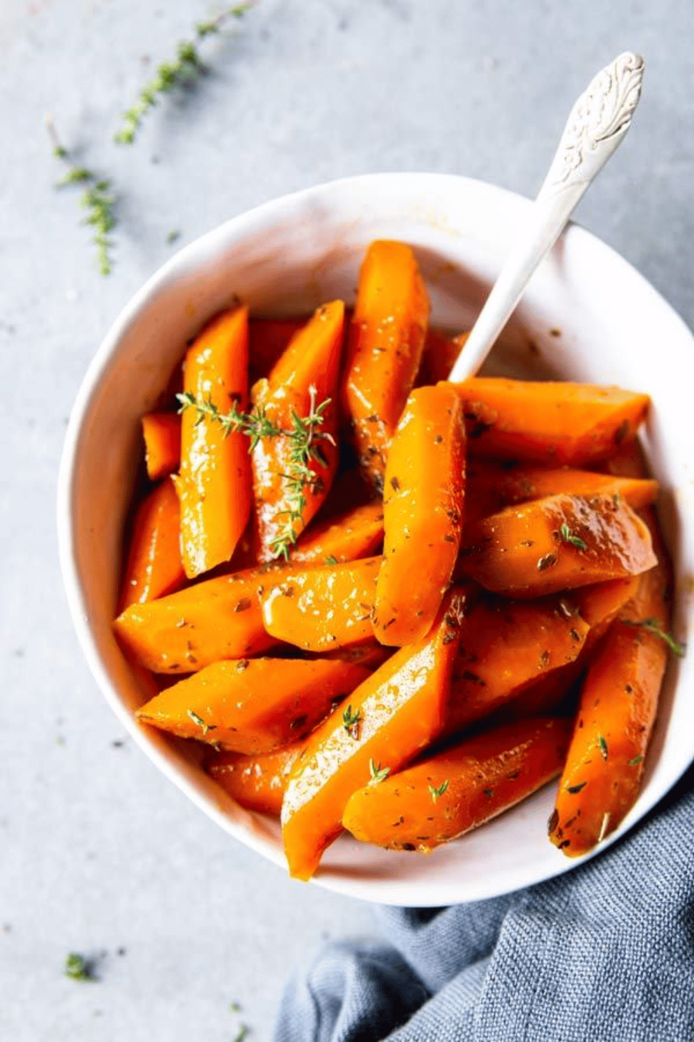 Glazed orange carrots in a white bowl, garnished with thyme sprigs.