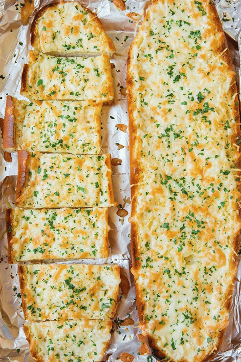 Slices of cheesy garlic bread garnished with parsley on a foil-lined baking sheet.