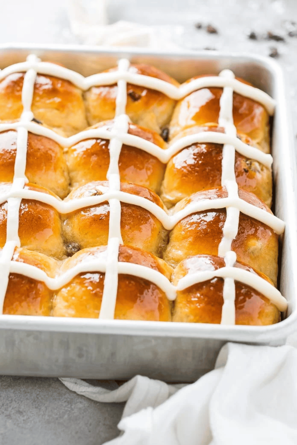 A baking pan filled with golden hot cross buns topped with a white icing cross.