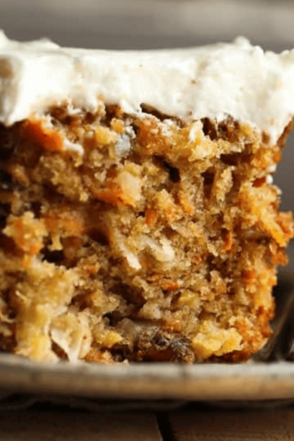 A slice of moist carrot cake with cream cheese frosting, showing the spiced interior.