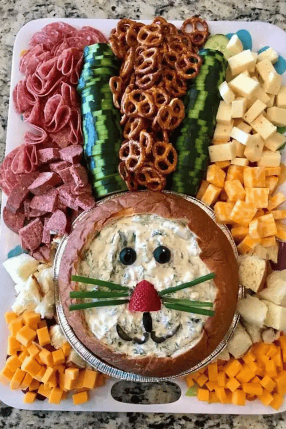 Colorful Easter charcuterie board featuring a bunny-shaped bread bowl, cheeses, meats, and pretzels.