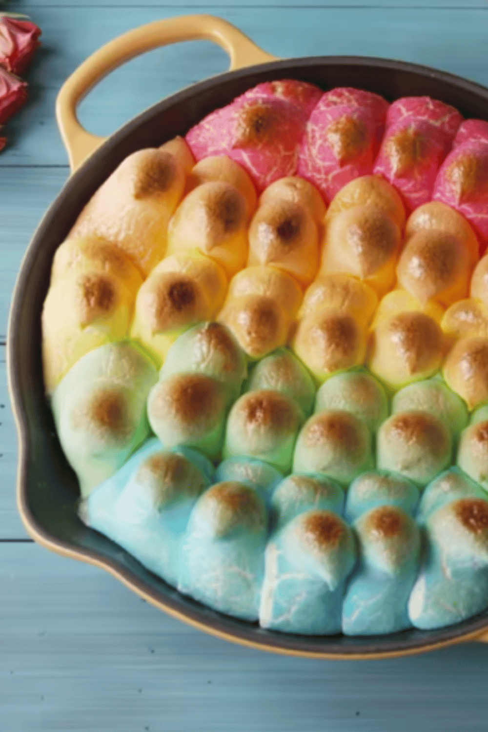 A skillet filled with toasted rainbow-colored Peeps over melted chocolate and graham crackers.