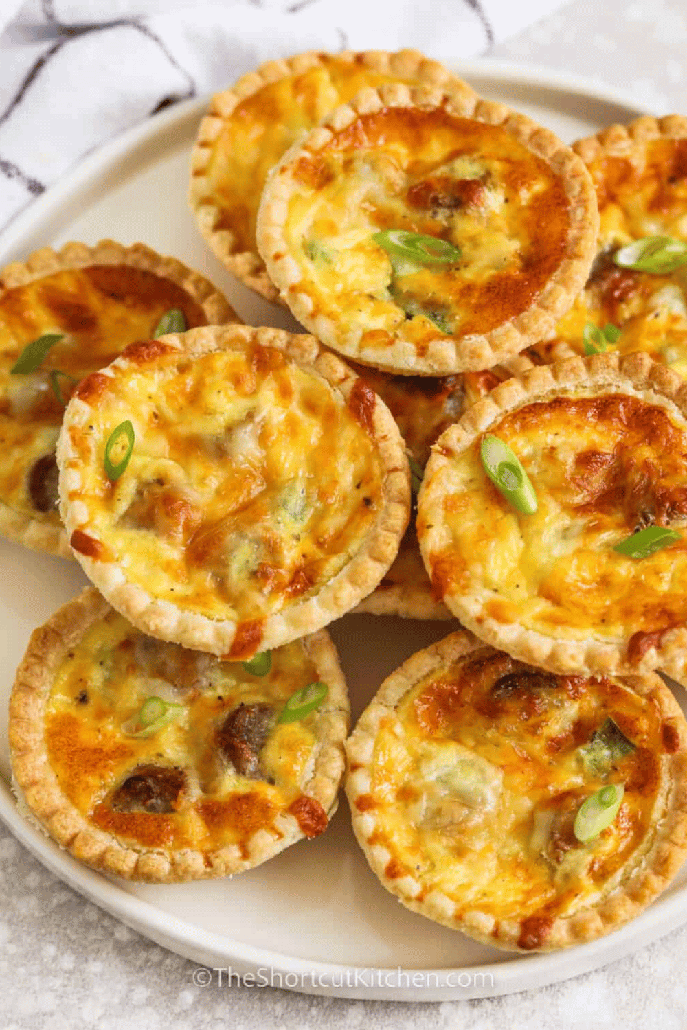 A plate of golden-brown mini quiche tarts topped with green onions.