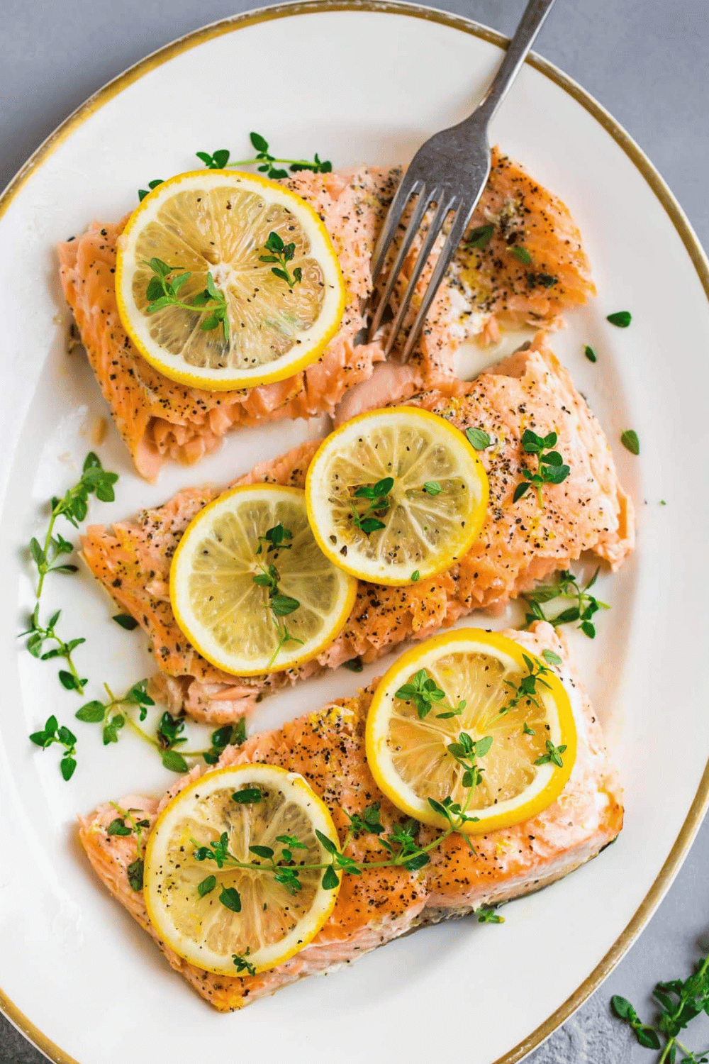 Lemon and herb salmon fillets topped with fresh lemon slices and thyme on a white plate.