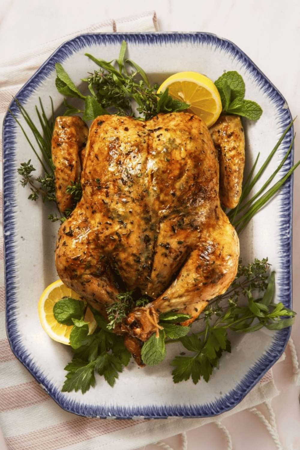 A golden roasted chicken garnished with lemon slices and fresh herbs on a serving platter.