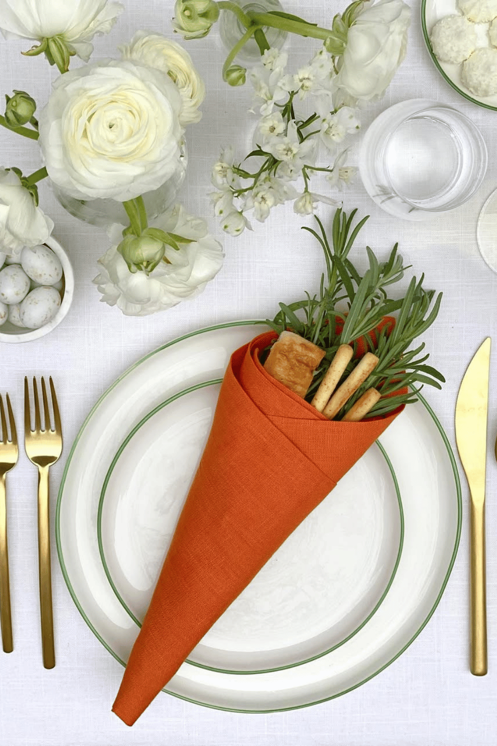 Creative Easter table ideas featuring a carrot-inspired napkin fold with breadsticks and fresh herbs.