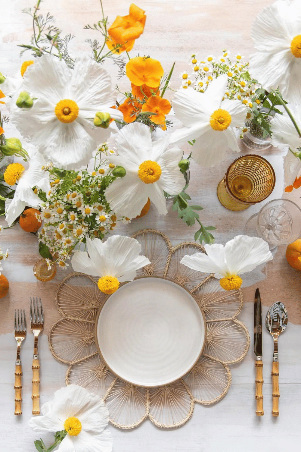 Bright and cheerful Easter dinner table setting with white daisies, orange blossoms, and bamboo cutlery.