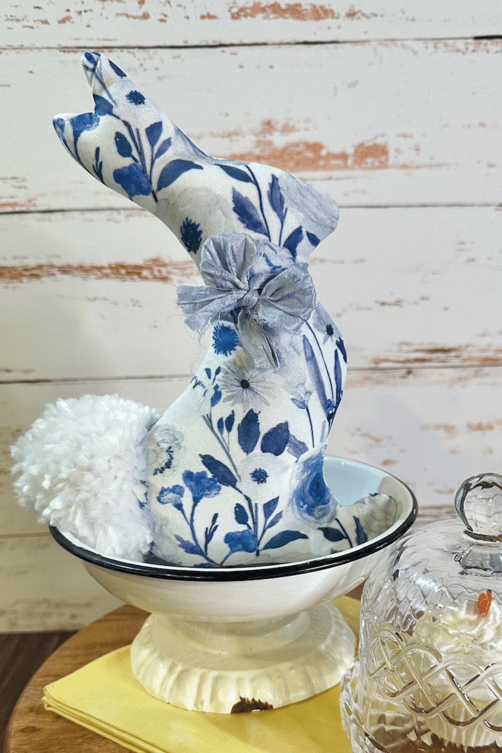 Blue and white fabric bunny with a pom-pom tail in a farmhouse setting.