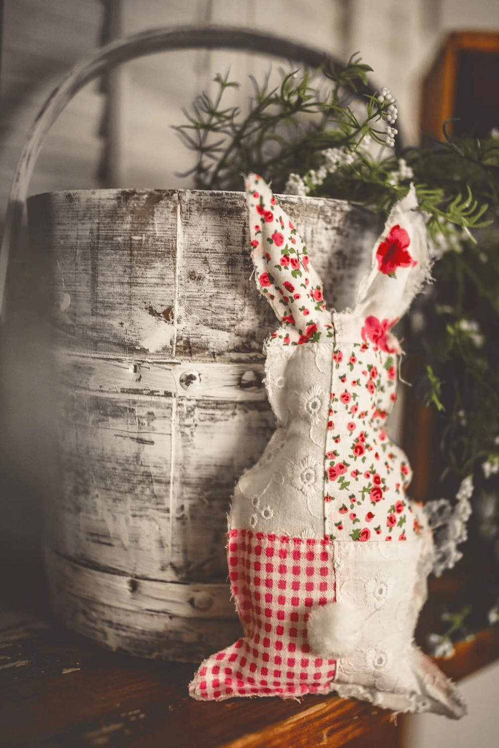 Patchwork fabric bunny leaning against a rustic bucket with greenery.