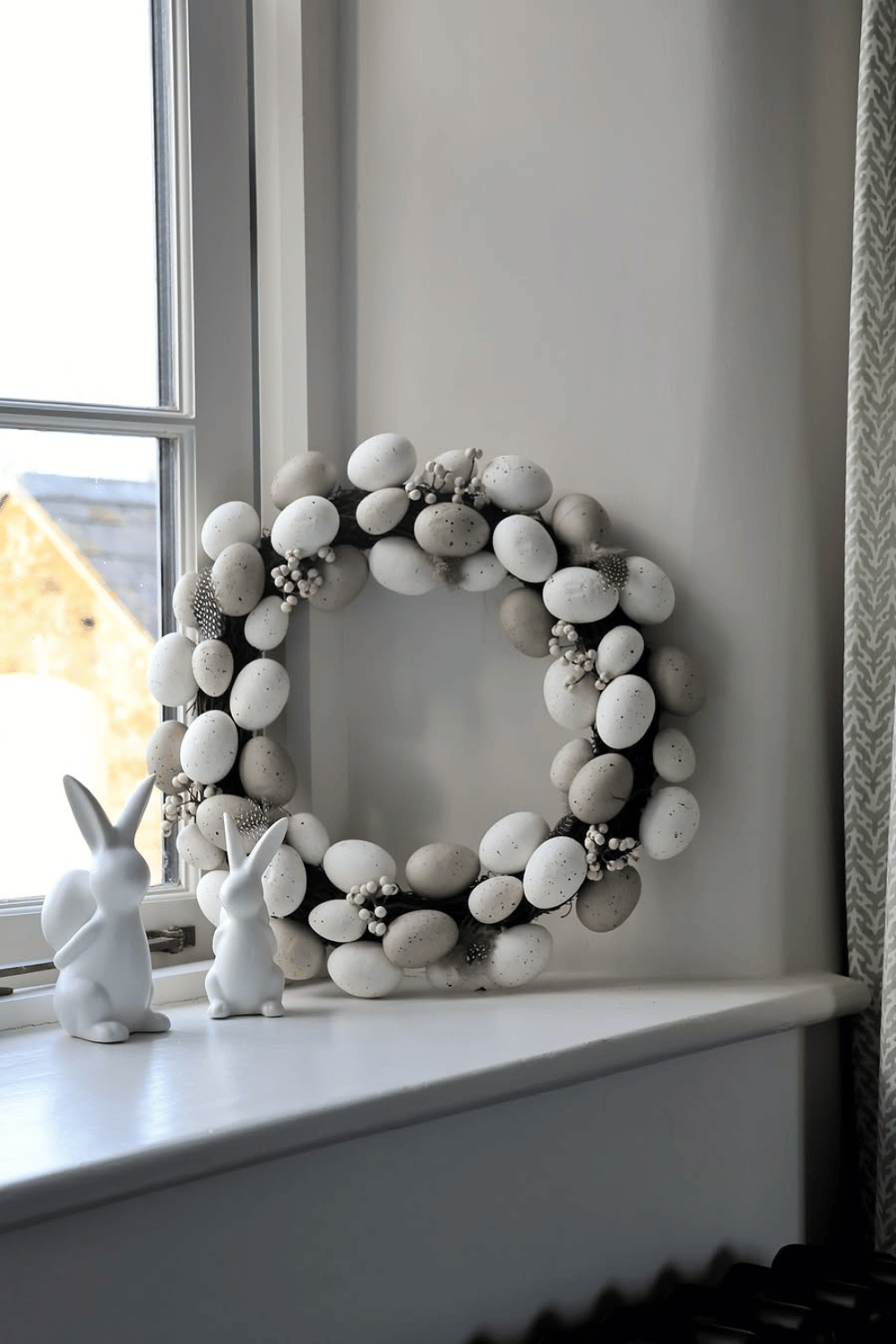 Neutral Easter egg wreath with white and beige eggs on a window sill.