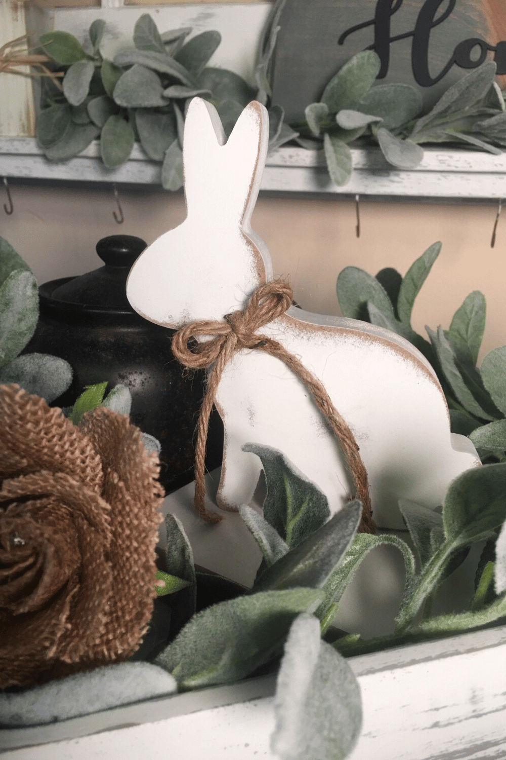 White wooden bunny tied with twine, surrounded by faux flowers.