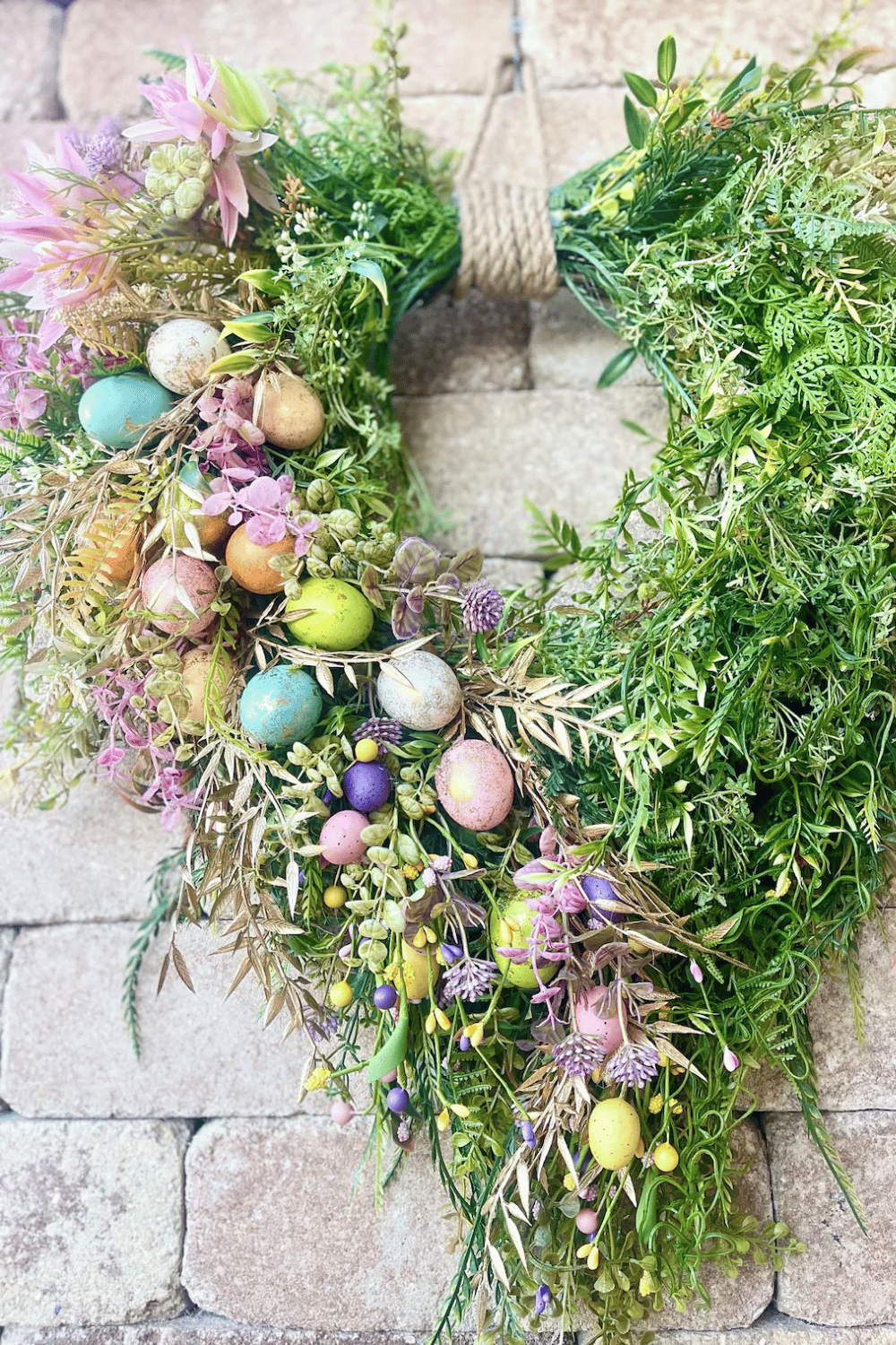 This Easter wreath features abundant greenery along with pastel-colored eggs and floral accents.