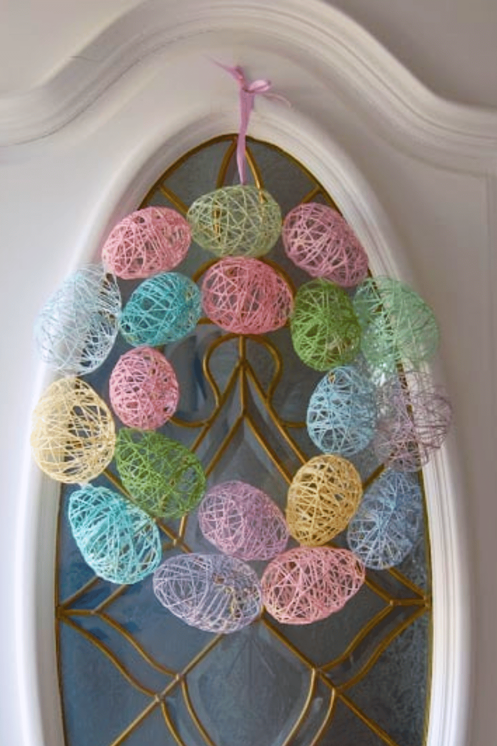 An Easter wreath featuring pastel eggs wrapped with string.