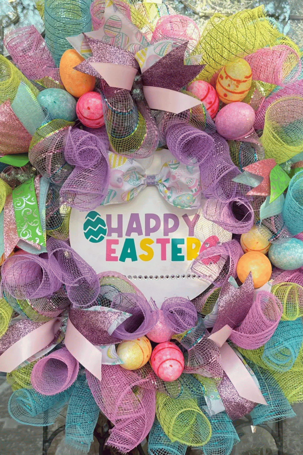 Easter wreath made with colorful mesh ribbon featuring eggs and an accompanying festive sign.