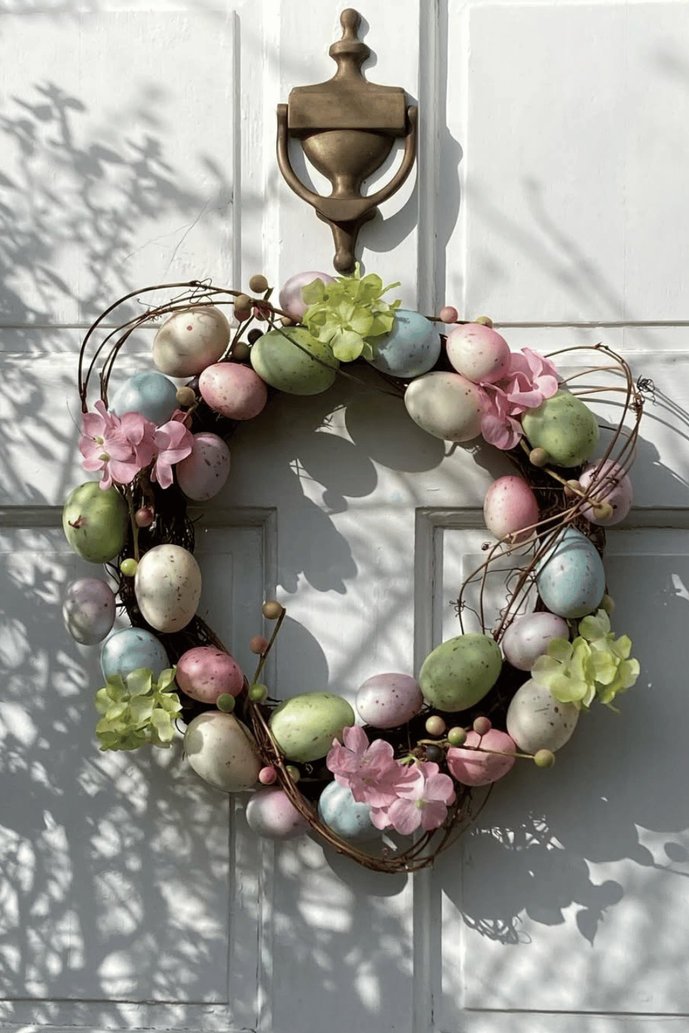 A grapevine base supports a charming rustic Easter wreath adorned with pastel-colored eggs and floral decorations.