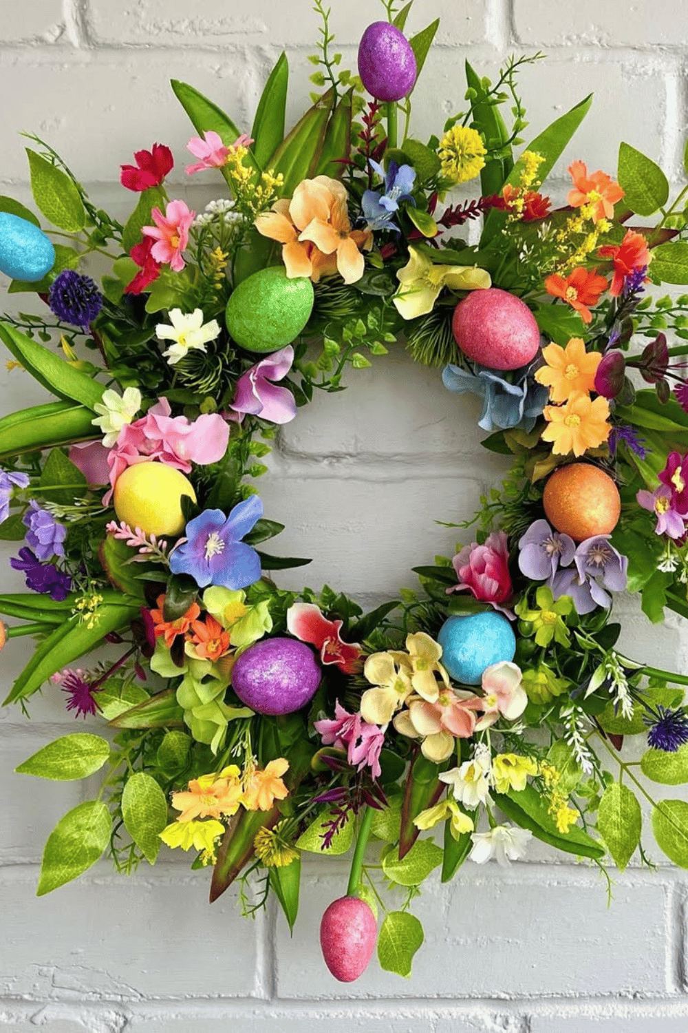 This Easter wreath features bright flowers and colorful eggs surrounded by vibrant greenery.