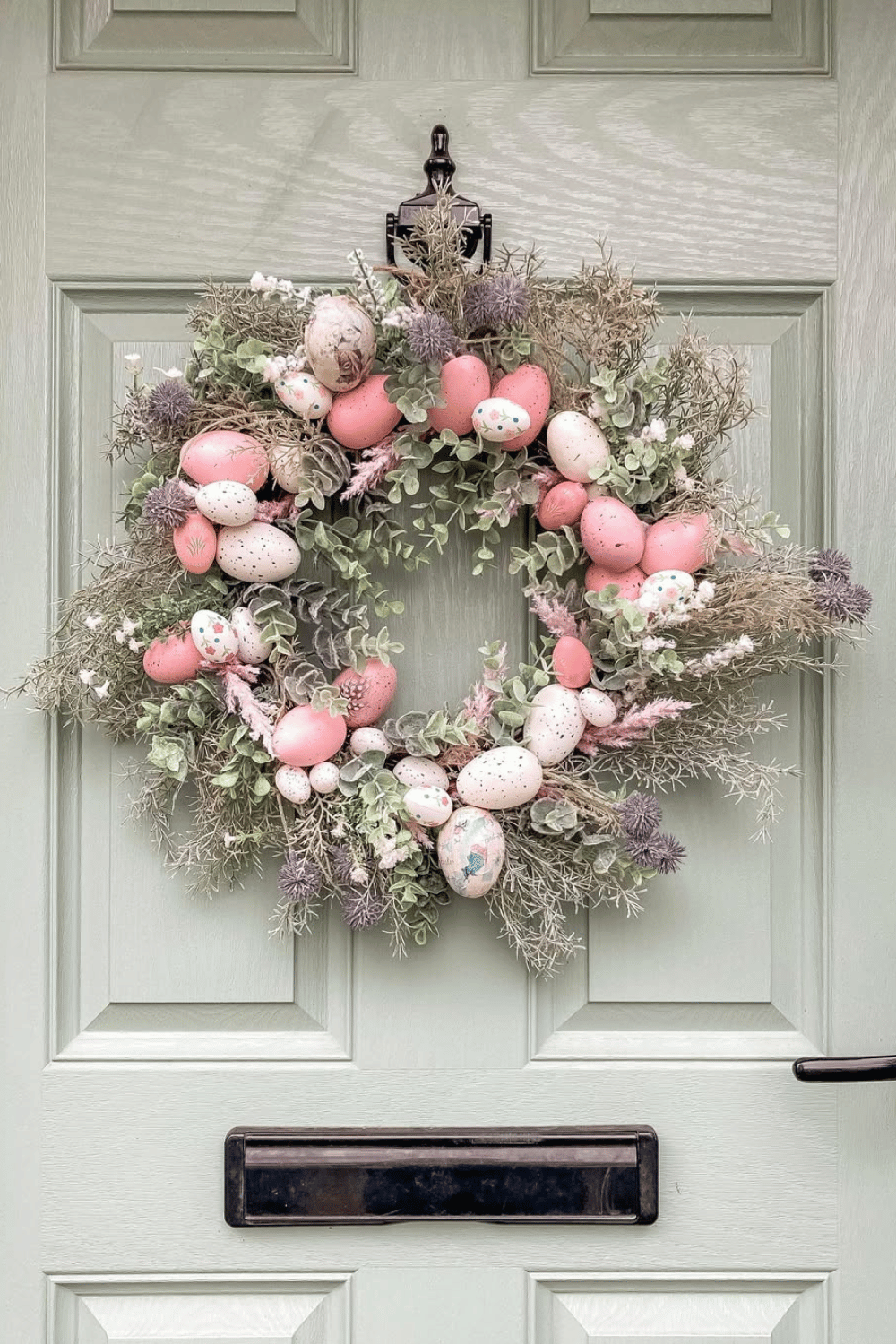 A speckled egg and greenery wreath rests on a soft pastel door.