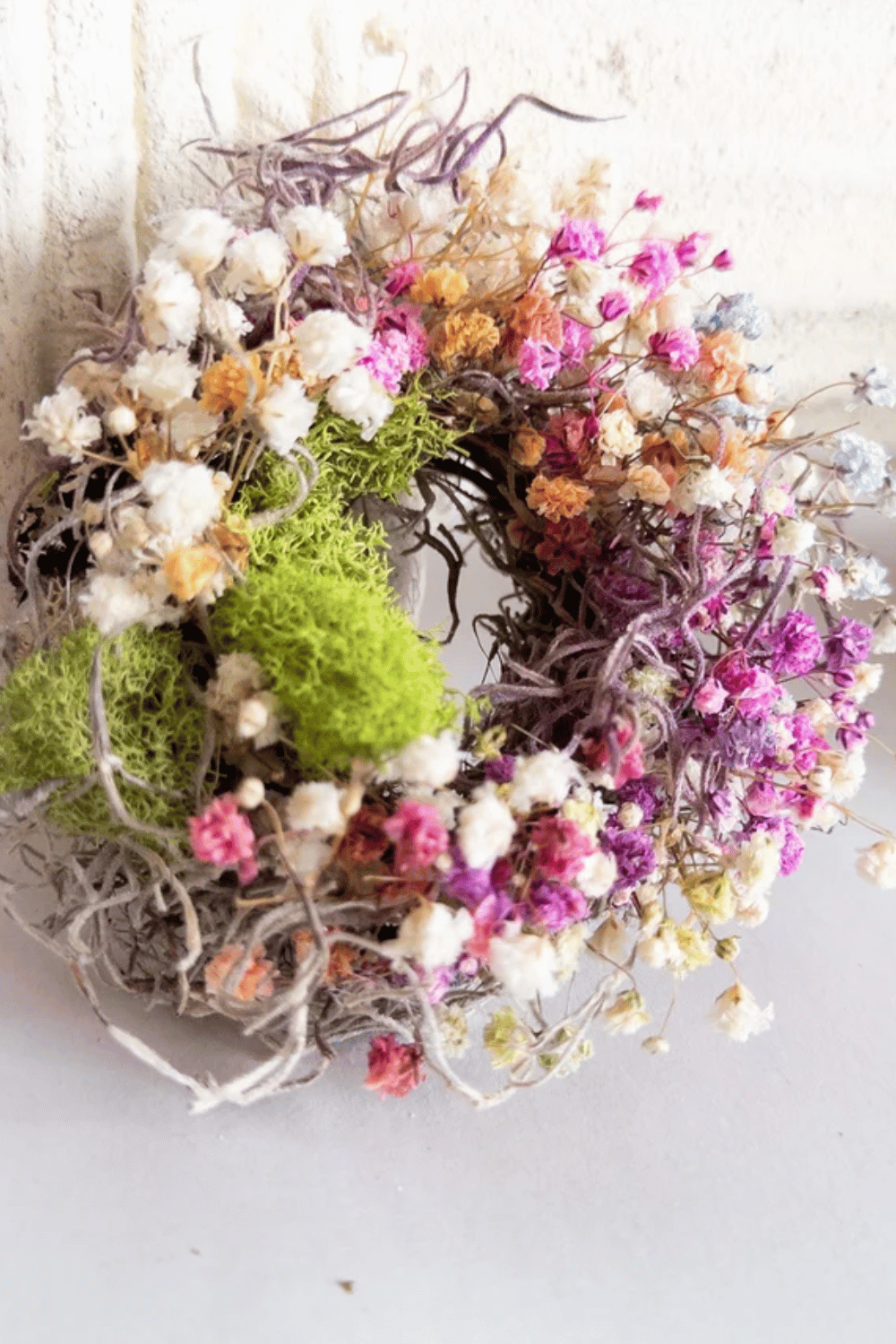 Easter wreath featuring dried flowers and moss surrounded by delicate blooms.