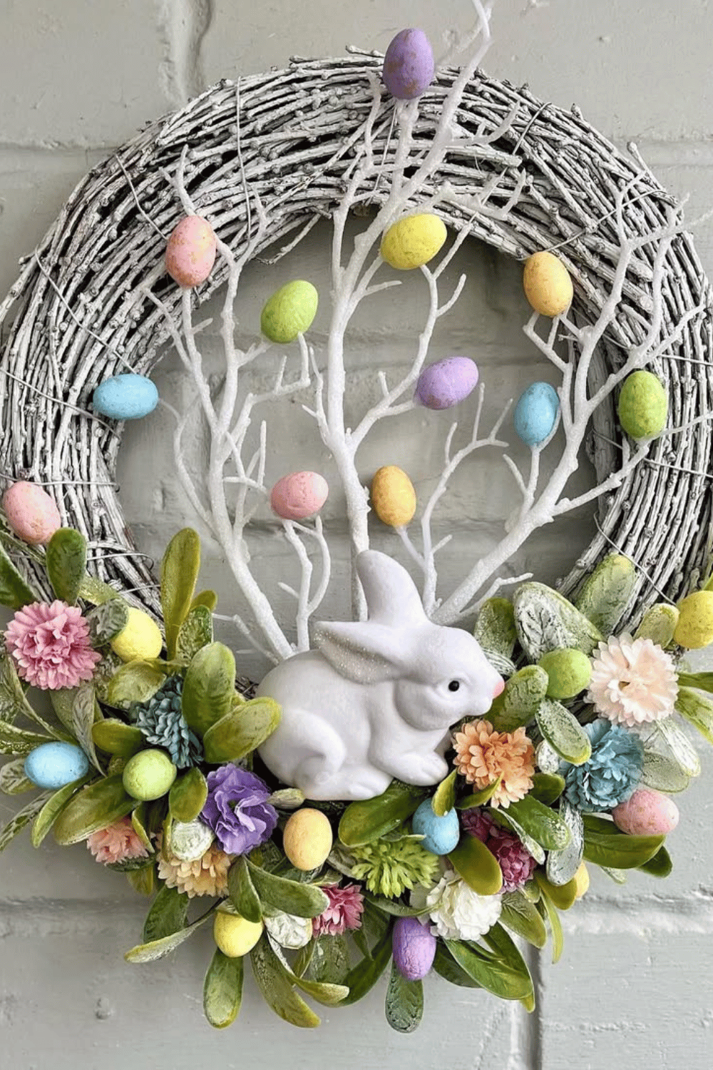 A white wreath from Easter displays pastel-colored eggs alongside a ceramic bunny figure.