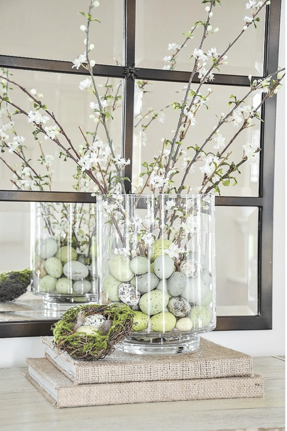 Clear glass vase filled with pastel Easter eggs and blossoming branches as spring table decoration
