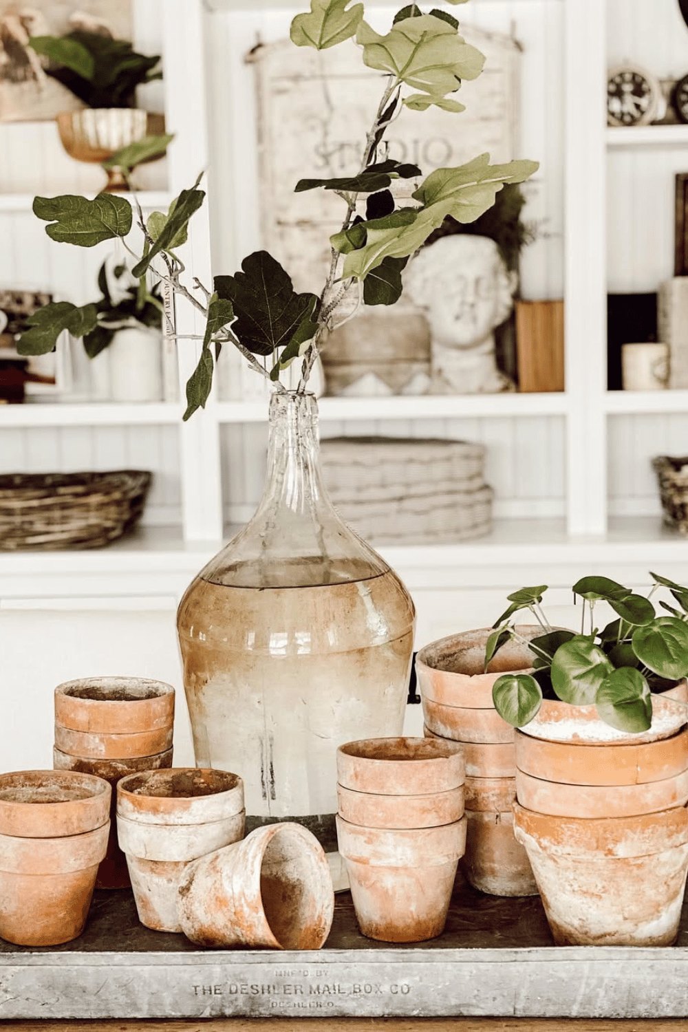 Large glass jug and stacked terracotta pots used as rustic spring dining table decor