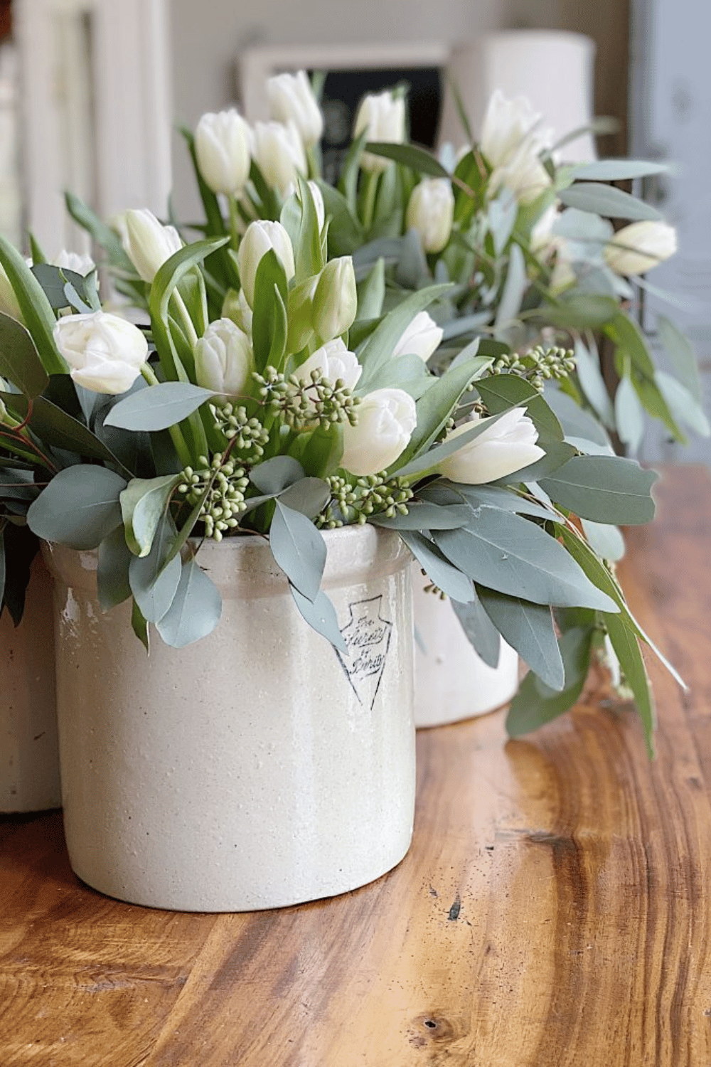Elegant white tulips and greenery styled in vintage crocks for spring table decor