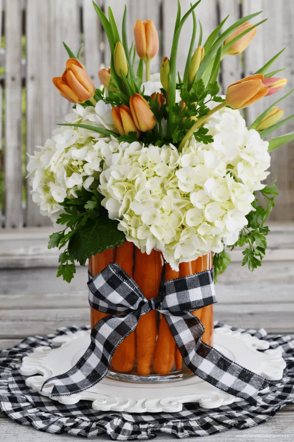 Clear vase with carrots, hydrangeas, orange tulips, and buffalo check ribbon as Easter table decor