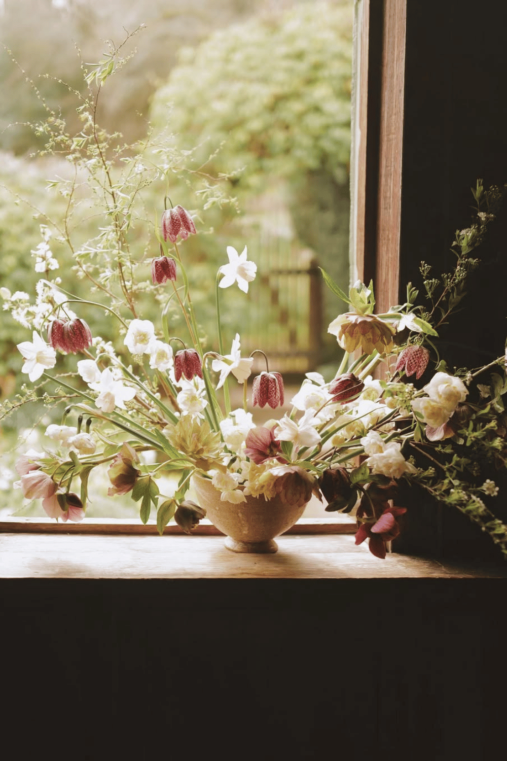 Wildflower and fritillary floral arrangement in a rustic bowl by a window