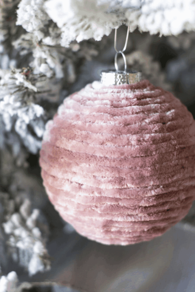 Fluffy pink velvet Christmas ornament hanging on a snowy tree