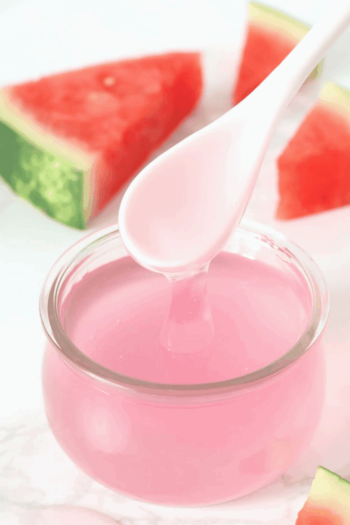 Glass jar of pink DIY serum with fresh watermelon slices in the background
