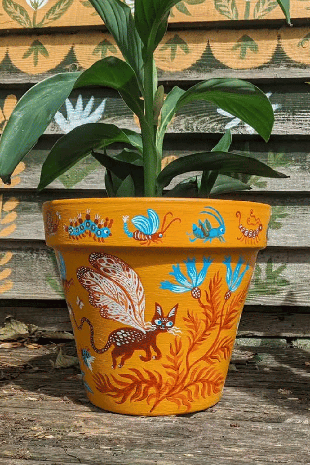 Folk art flower pot painted with whimsical animals and bright blue flowers